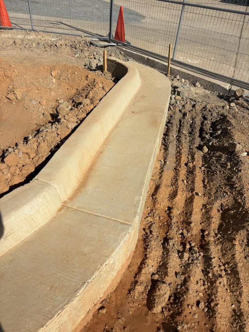Freshly poured concrete curb running along a graded commercial site