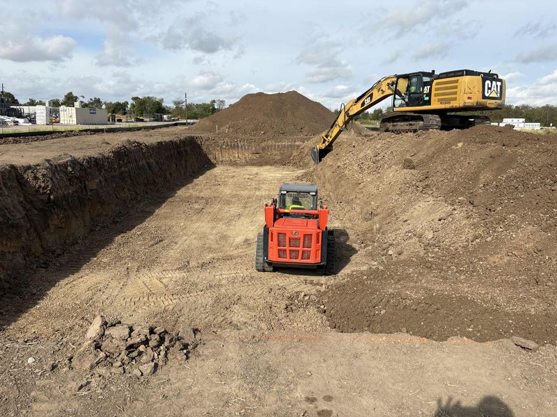 Excavator on the spoil pile above a track loader working inside a large commercial excavation